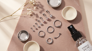 G23 titanium helix piercing jewelry curation — graduated studs, captive bead, seam ring, and huggie hoop with sterile saline on dusty rose stone, SSZ Piercing