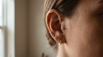 Close-up of a curated ear with helix, conch and lobe cartilage piercings in minimalist titanium and gold jewelry