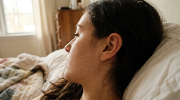 Woman resting in bed on a pillow with a healed cartilage ear piercing visible, illustrating how to sleep without pressure on a new piercing