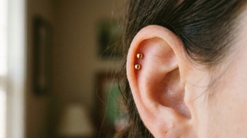 Close-up of an upper ear with two matching gold helix studs set close together in a snakebite helix
