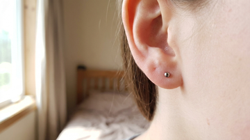 Extreme close-up of a calm healthy ear with a minimalist implant-grade titanium stud and clear skin