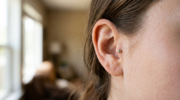 Close-up of an ear with a delicate gold tragus gem stud on the cartilage nub in front of the ear canal