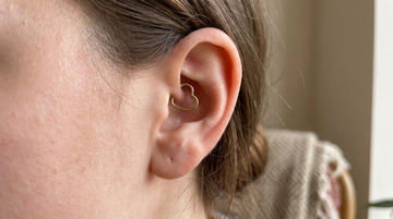 Close-up of an ear with a daith piercing wearing a delicate gold heart-shaped ring in the inner cartilage fold