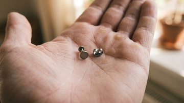 Palm holding a flat disc labret back next to a butterfly clutch back, comparing earring backings