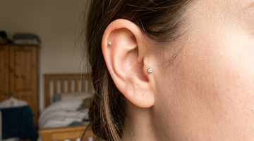 Close-up of an ear with a helix stud high on the rim and a tragus gem stud below in a starter curated stack