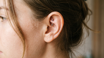 Rook piercing with a small titanium curved barbell, its bead ends peeking over the anti-helix ridge of the ear