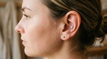 Conch piercing with a crystal cluster titanium stud in the center shell of the ear, with a gold stud on the lobe