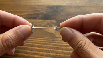 The two parts of a threadless titanium earring held apart — flat-back post on one side, crystal top with its pin on the other