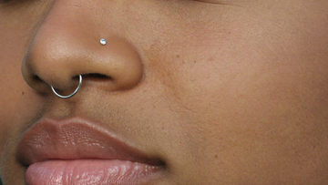 Double nose piercing — a crystal stud above and a slim silver hoop below on the same nostril
