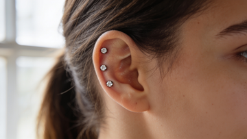 Triple helix piercing — three titanium crystal studs in an even row along the upper cartilage rim of the ear