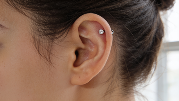 Mid helix piercing — a single titanium crystal flat-back stud on the outer cartilage rim of the ear