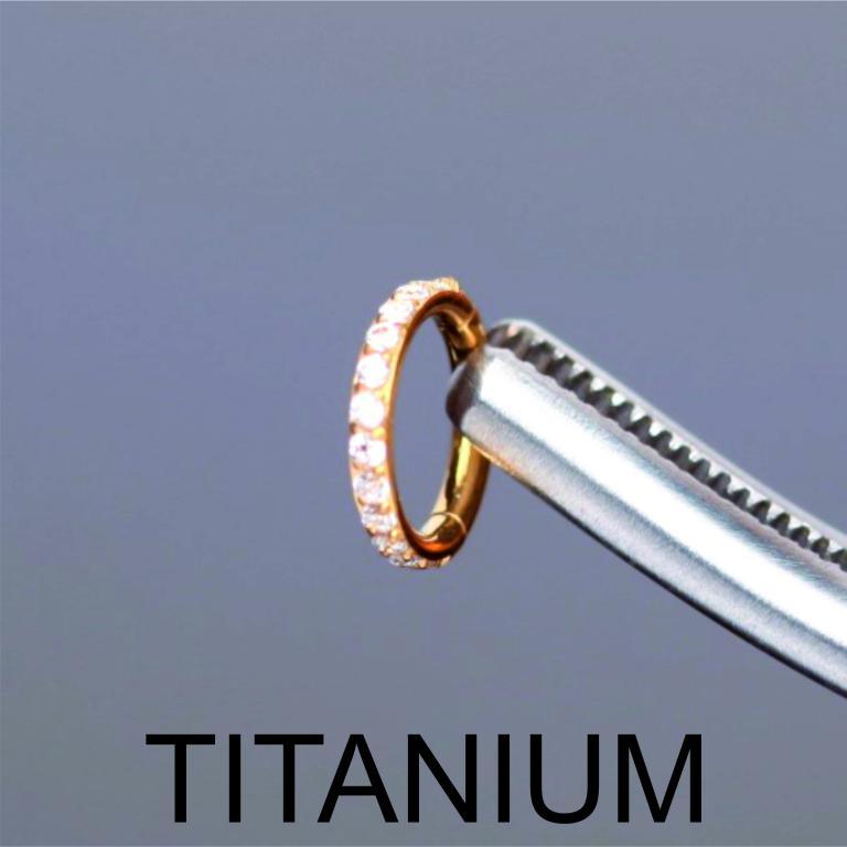 Close-up of a gold titanium zircon hinged clicker hoop ring showcasing crystal