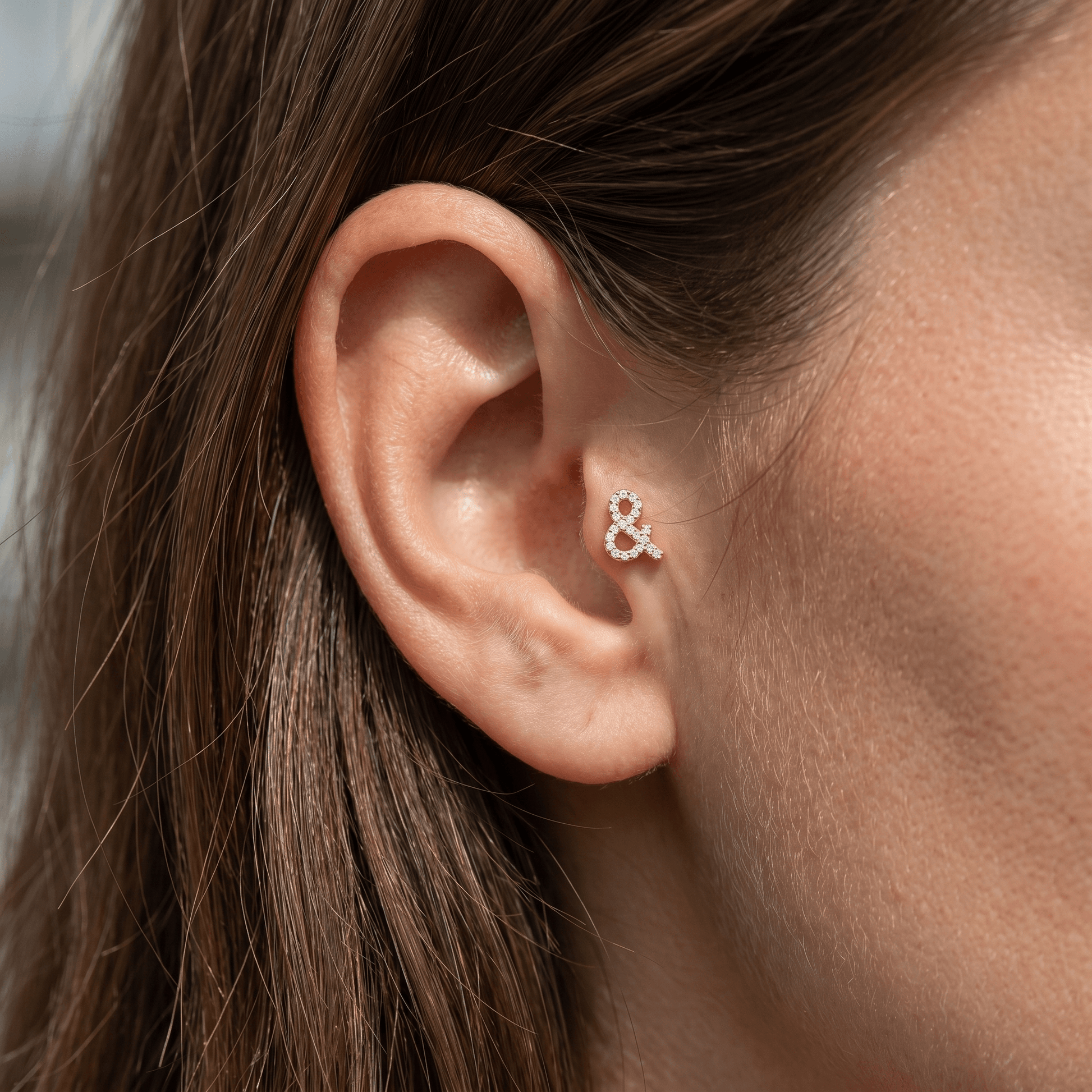 Gold titanium ampersand zircon piercing stud worn in a female piercing.