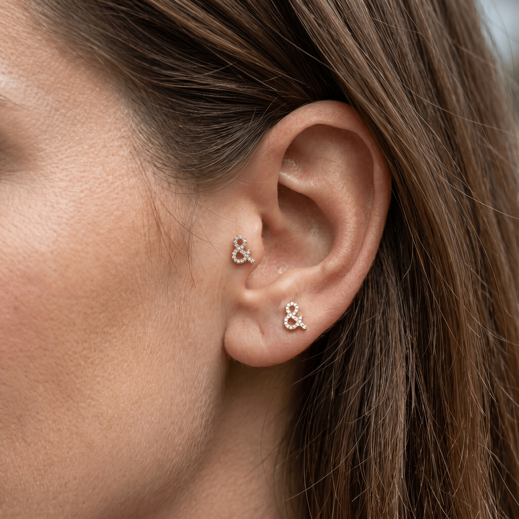 Two gold titanium ampersand zircon piercing studs worn in female and piercings.