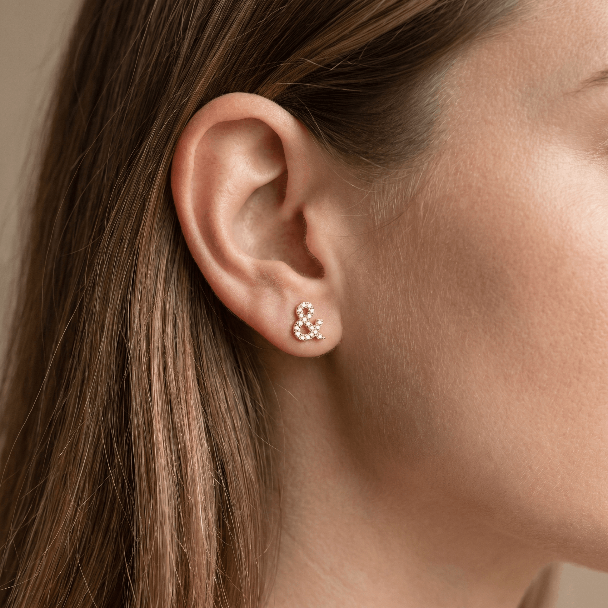 Gold titanium ampersand zircon piercing stud worn elegantly in a female ear.