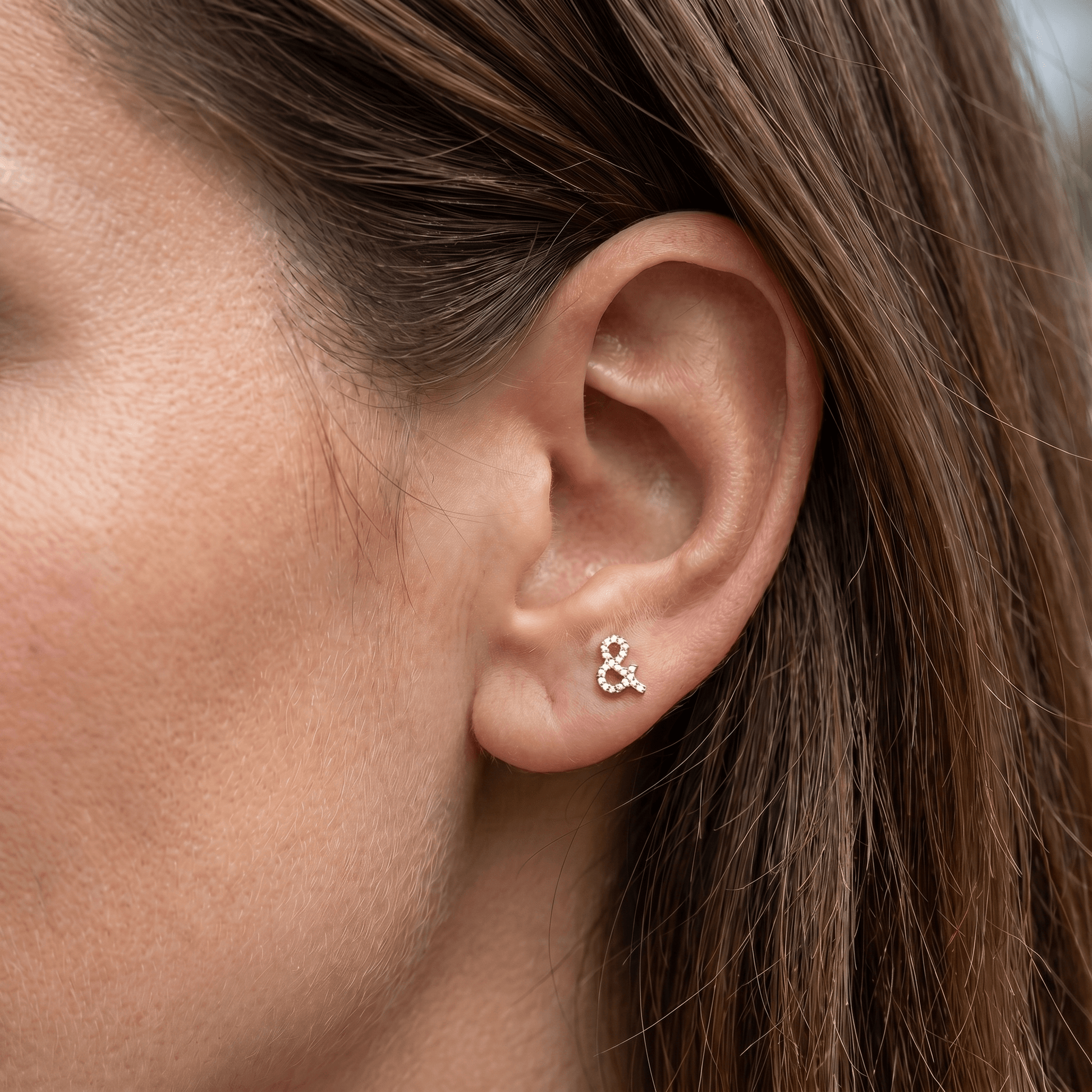 Gold titanium ampersand zircon piercing stud worn in a female anti tragus piercing.