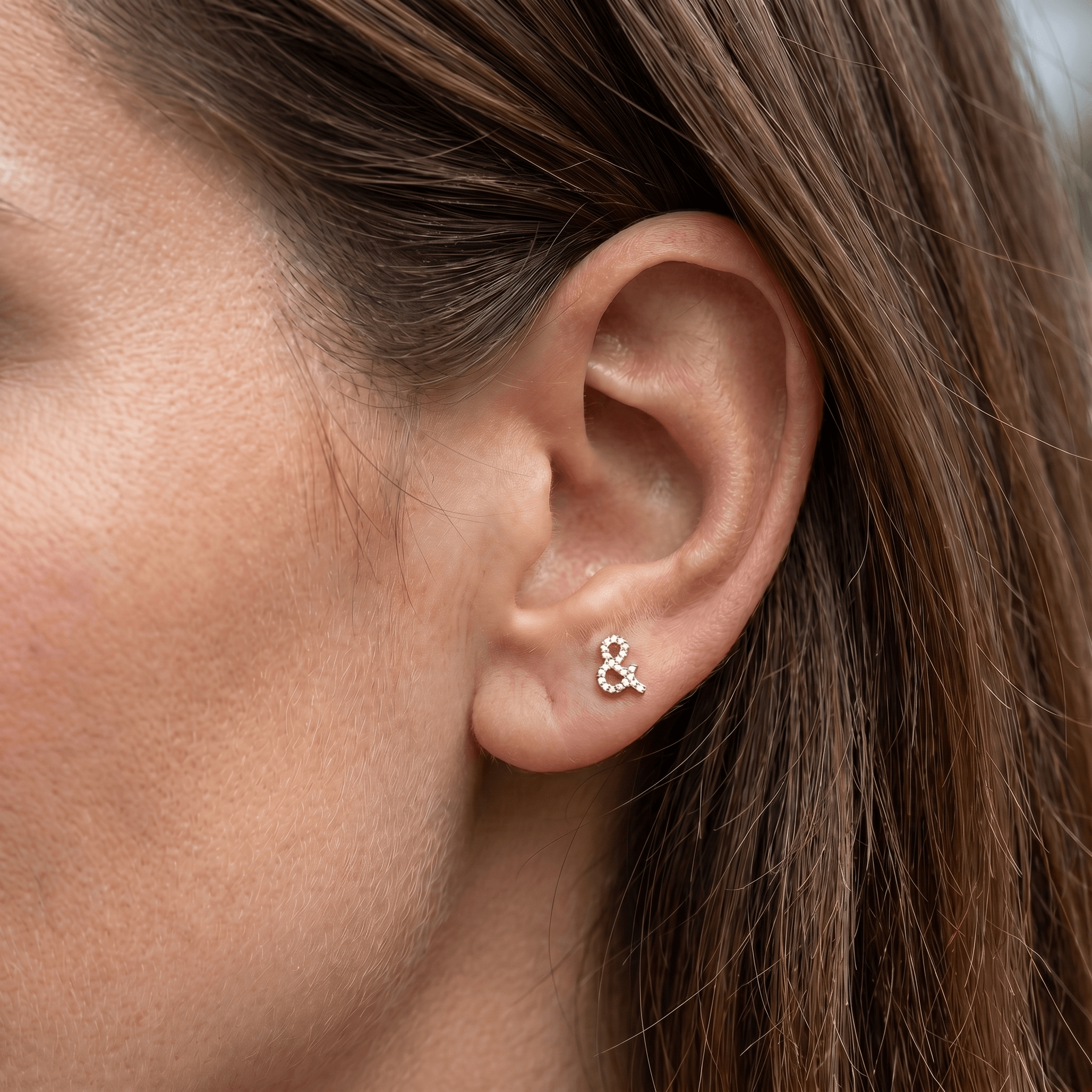 Gold titanium ampersand zircon piercing stud worn in a female anti tragus piercing.