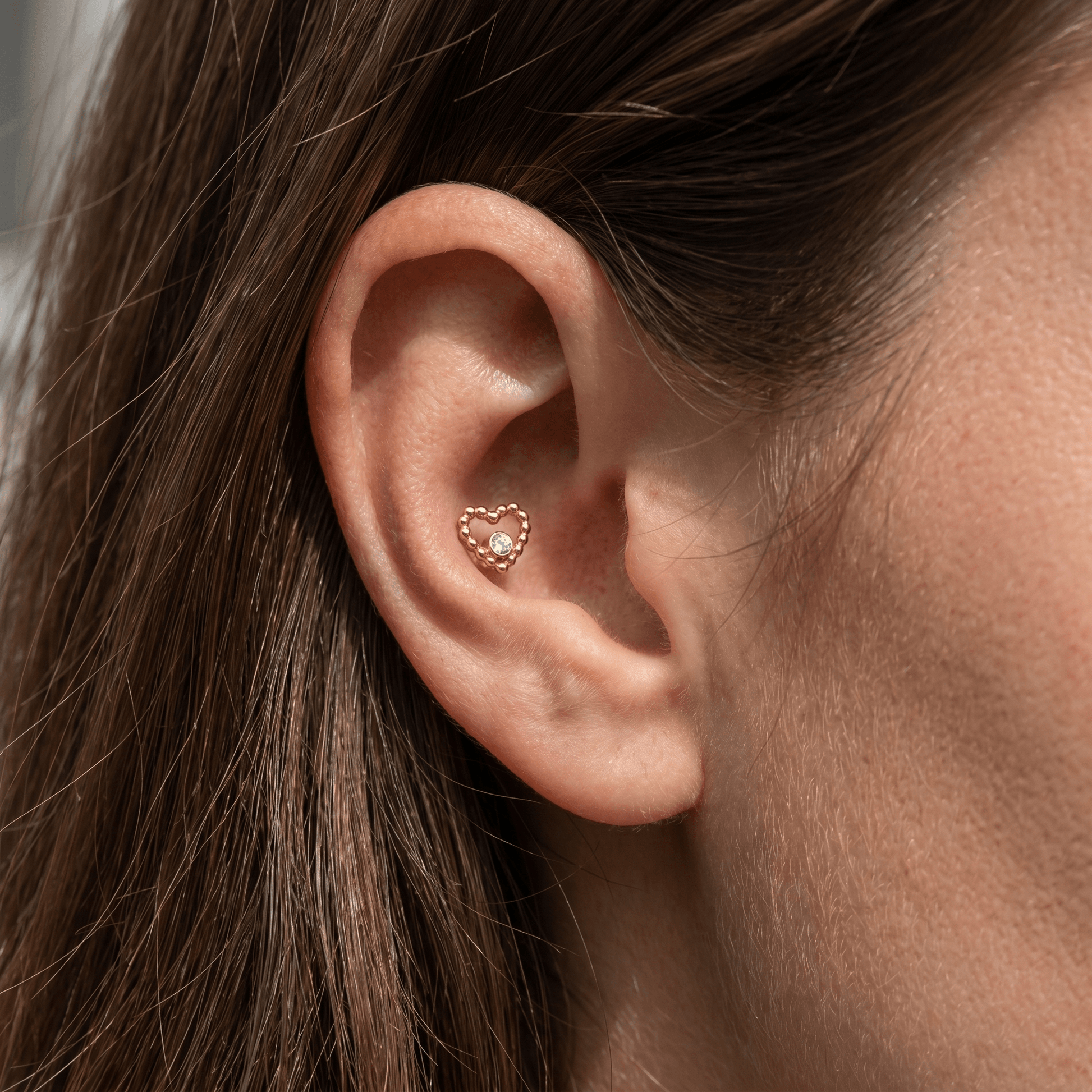 Gold titanium beaded heart piercing stud worn beautifully in a female conch ear piercing.