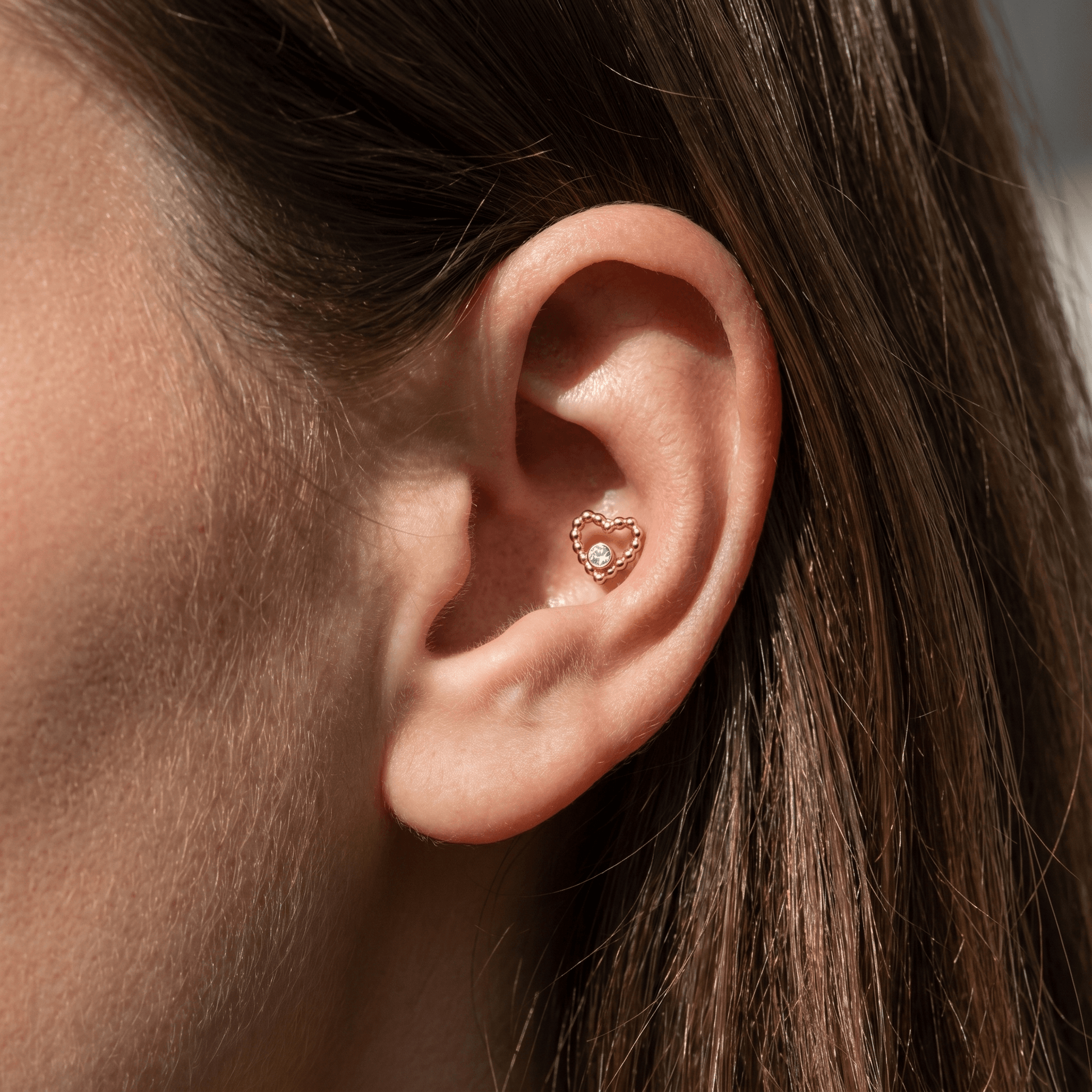 Gold titanium beaded heart stud worn elegantly in a female ear.