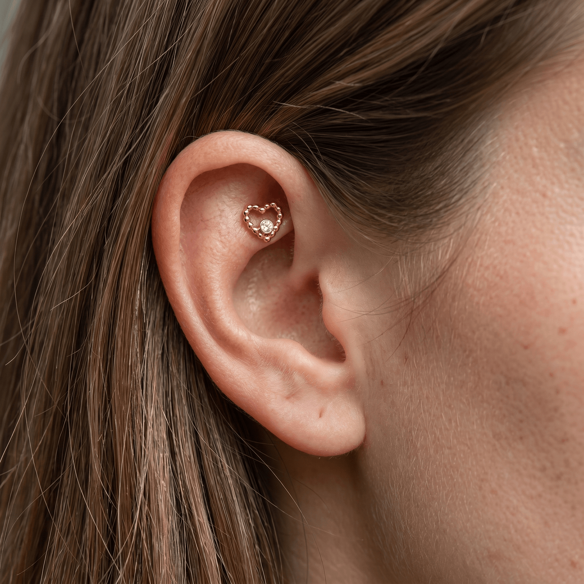 Profile view of a gold titanium beaded heart faux piercing stud worn