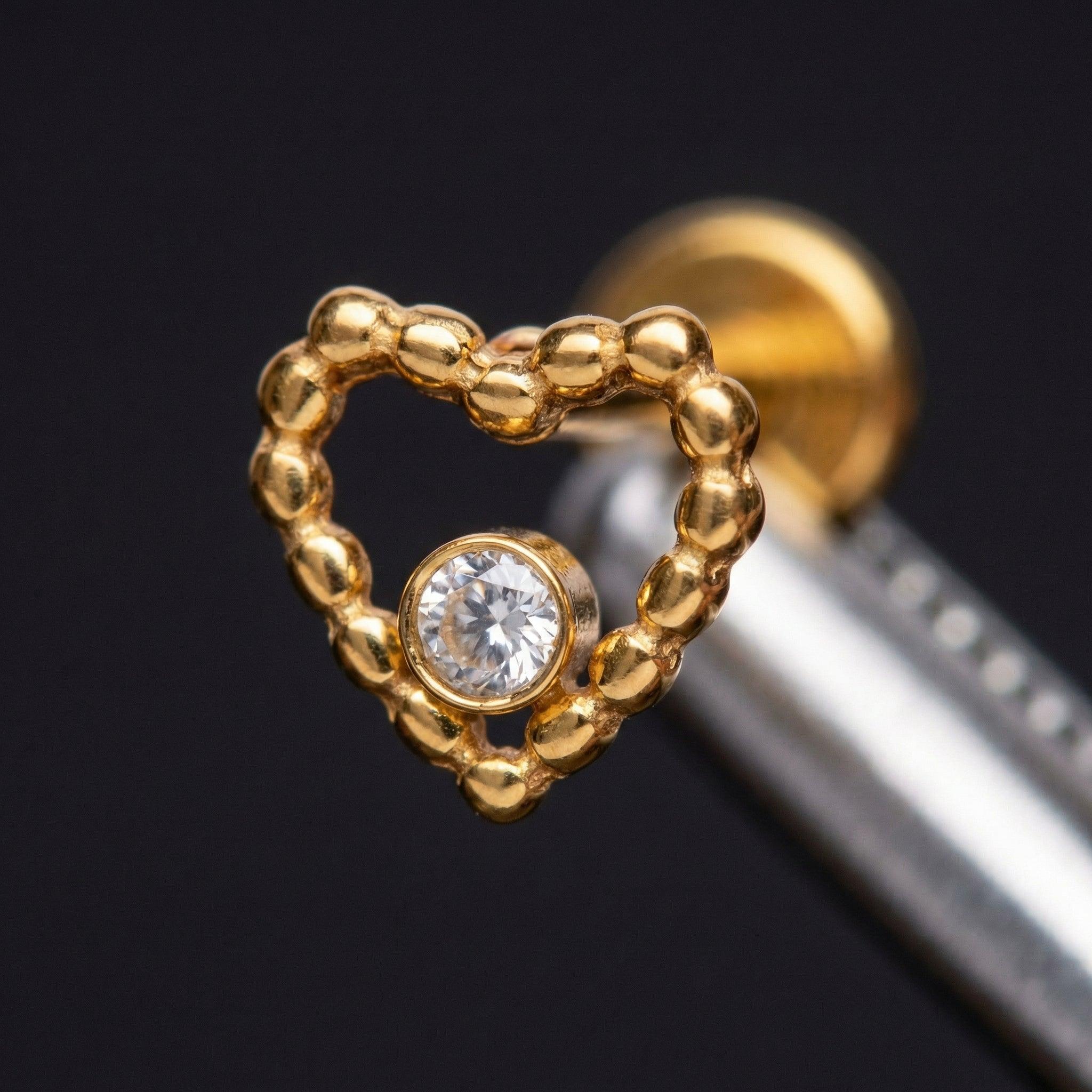Macro close-up of a gold titanium beaded heart cartilage piercing stud showing
