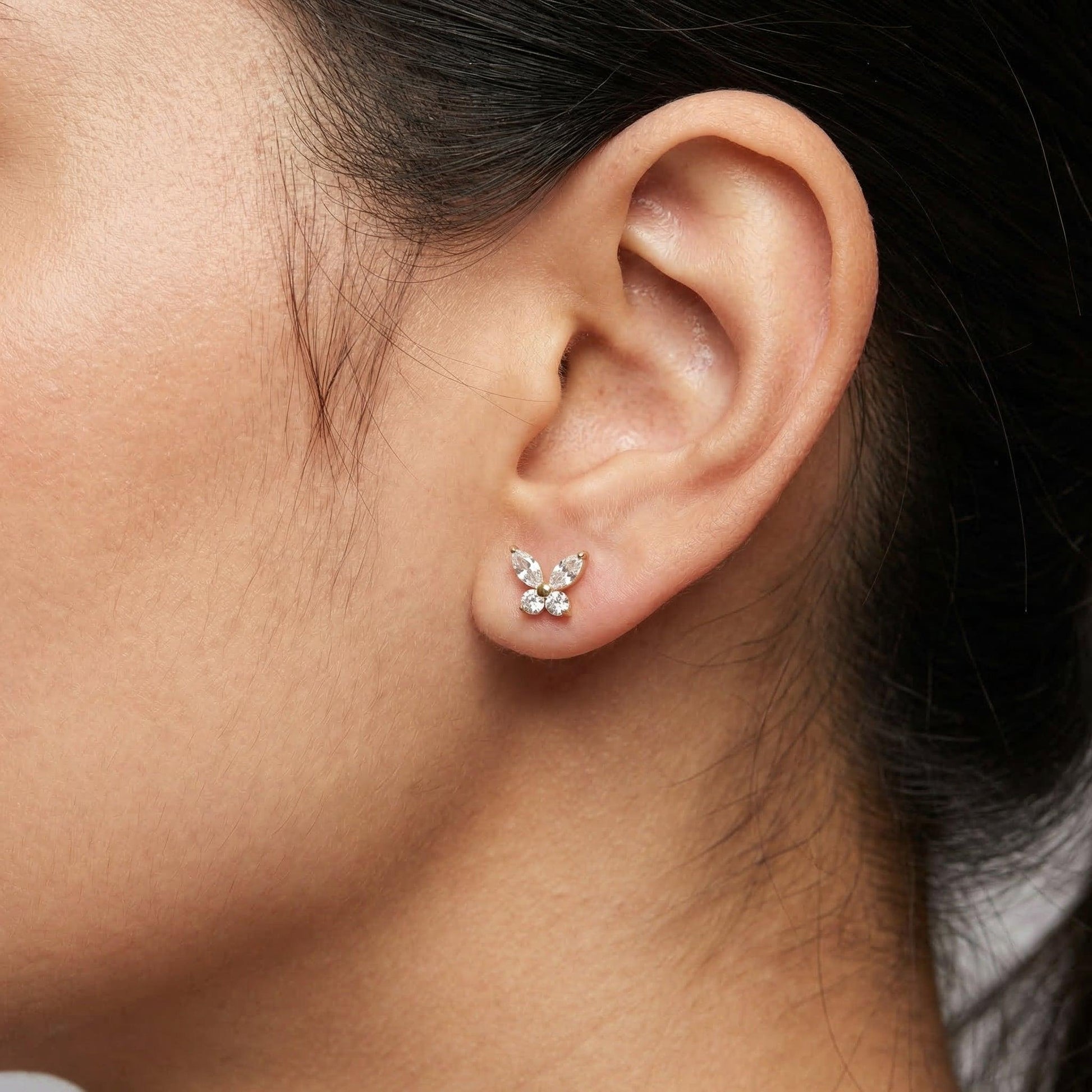 Gold titanium butterfly piercing stud worn in a female .