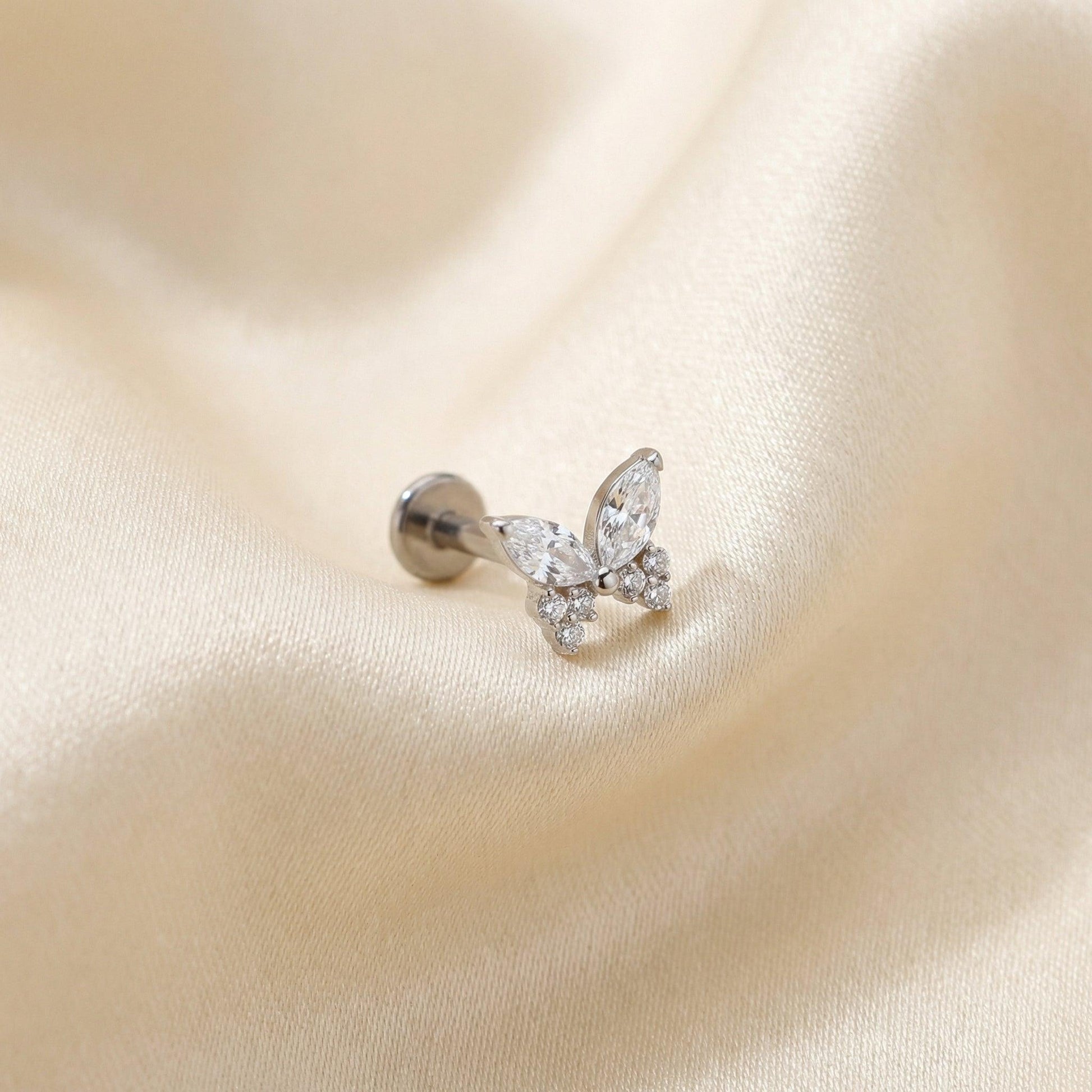 Silver titanium butterfly zircon cartilage stud lying flat on a silk fabric.