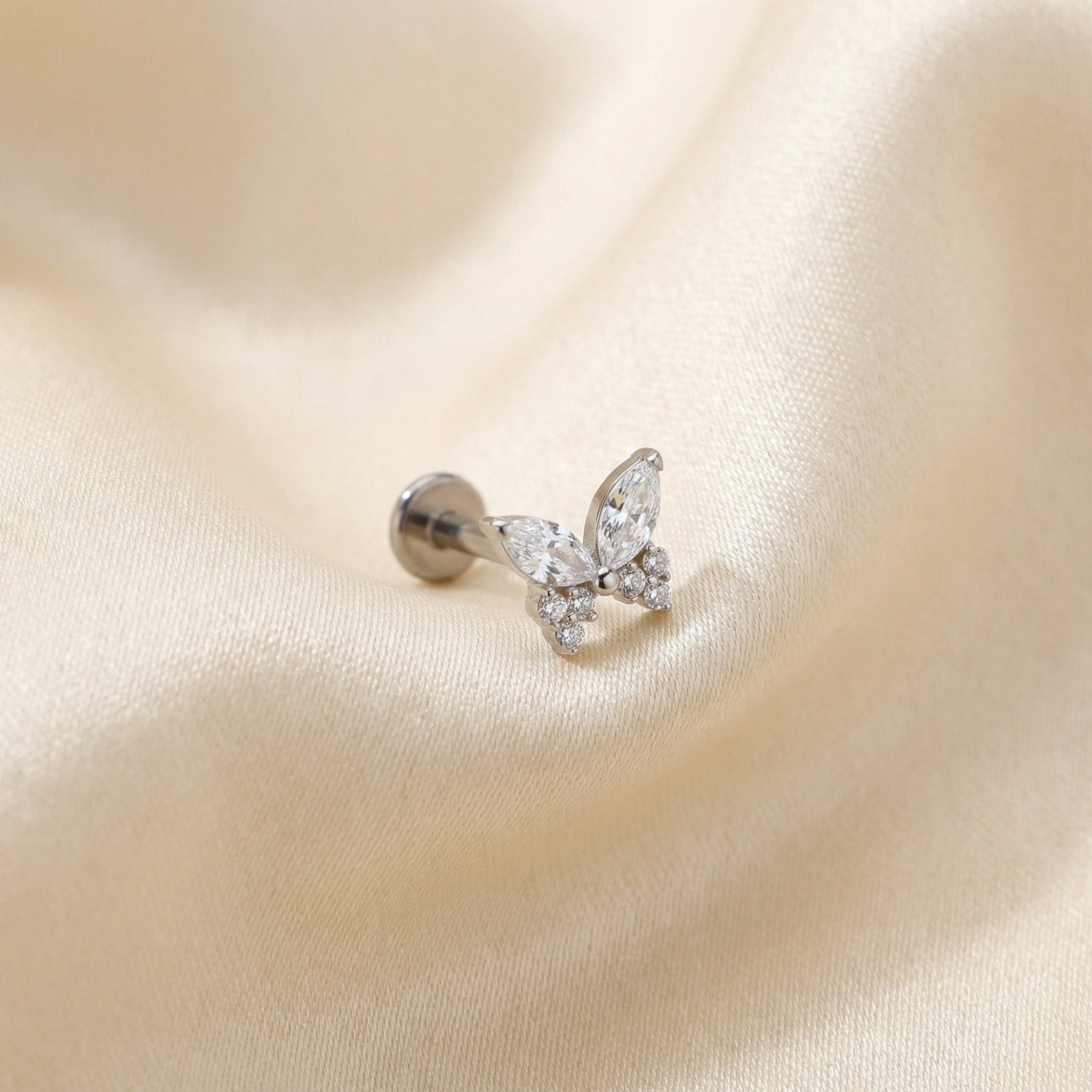 Silver titanium butterfly zircon cartilage stud lying flat on a silk fabric.