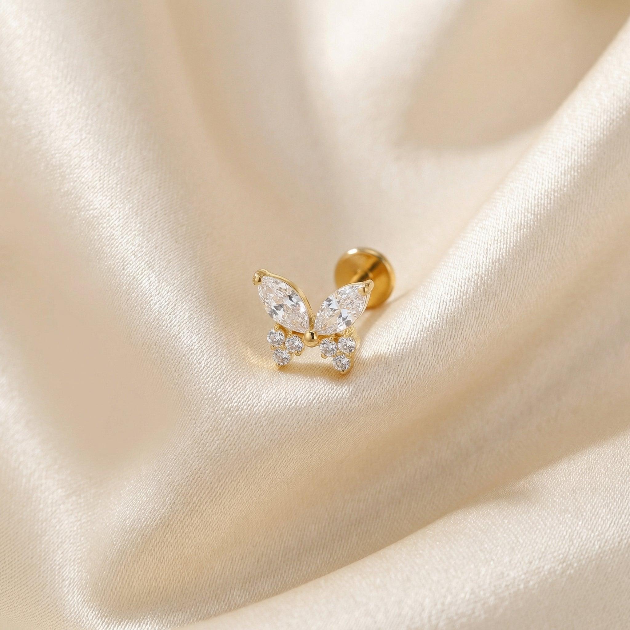 Gold titanium butterfly zircon cartilage stud lying flat on a silk fabric.