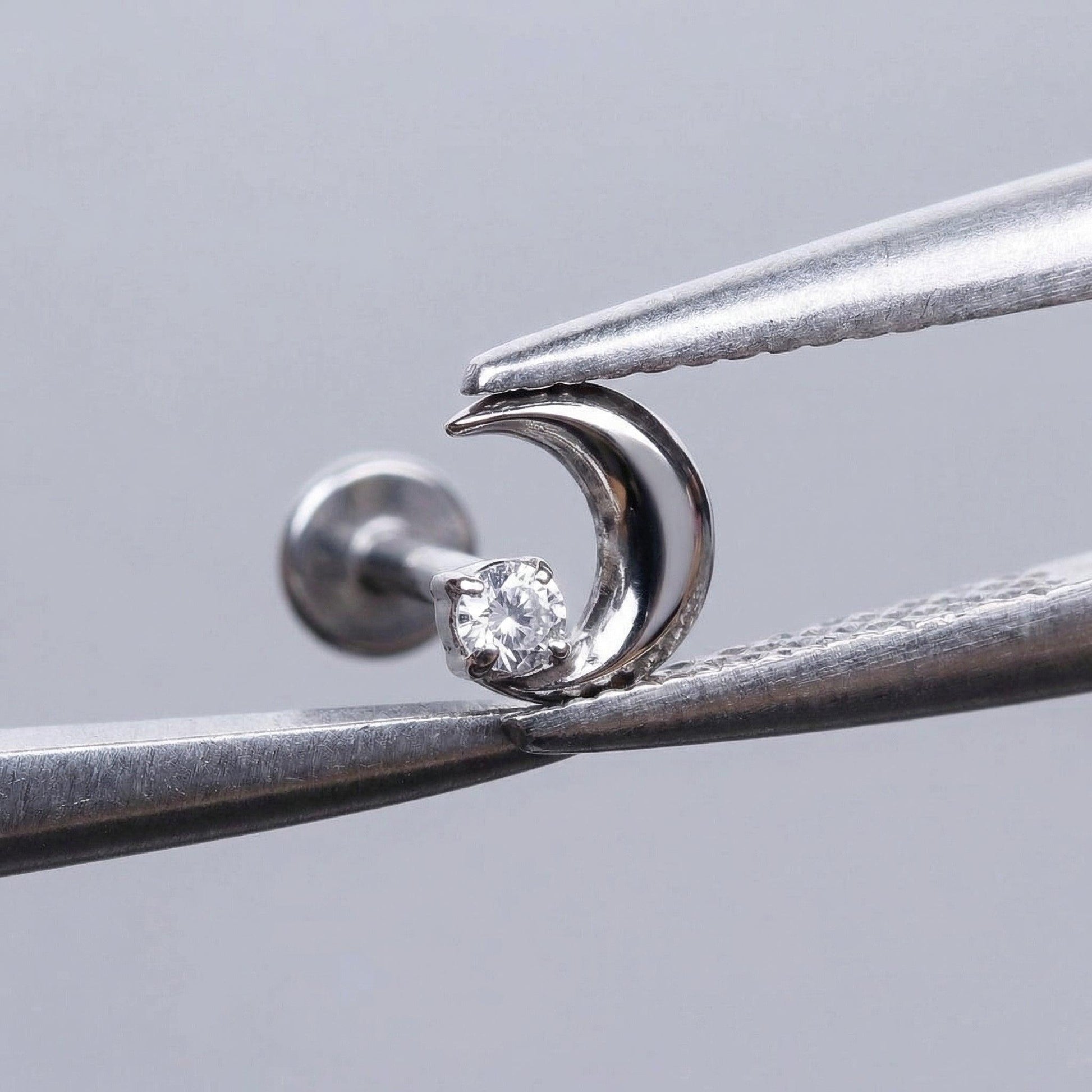 Silver celestial cartilage stud held securely by metal tweezers.