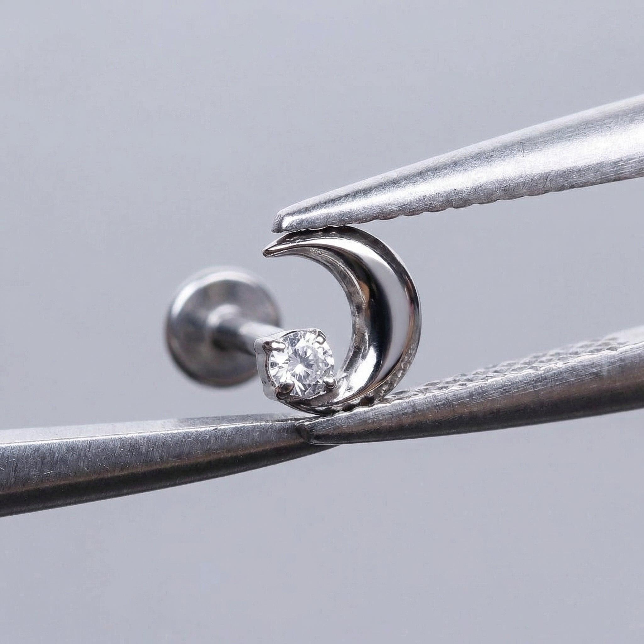 Silver celestial cartilage stud held securely by metal tweezers.