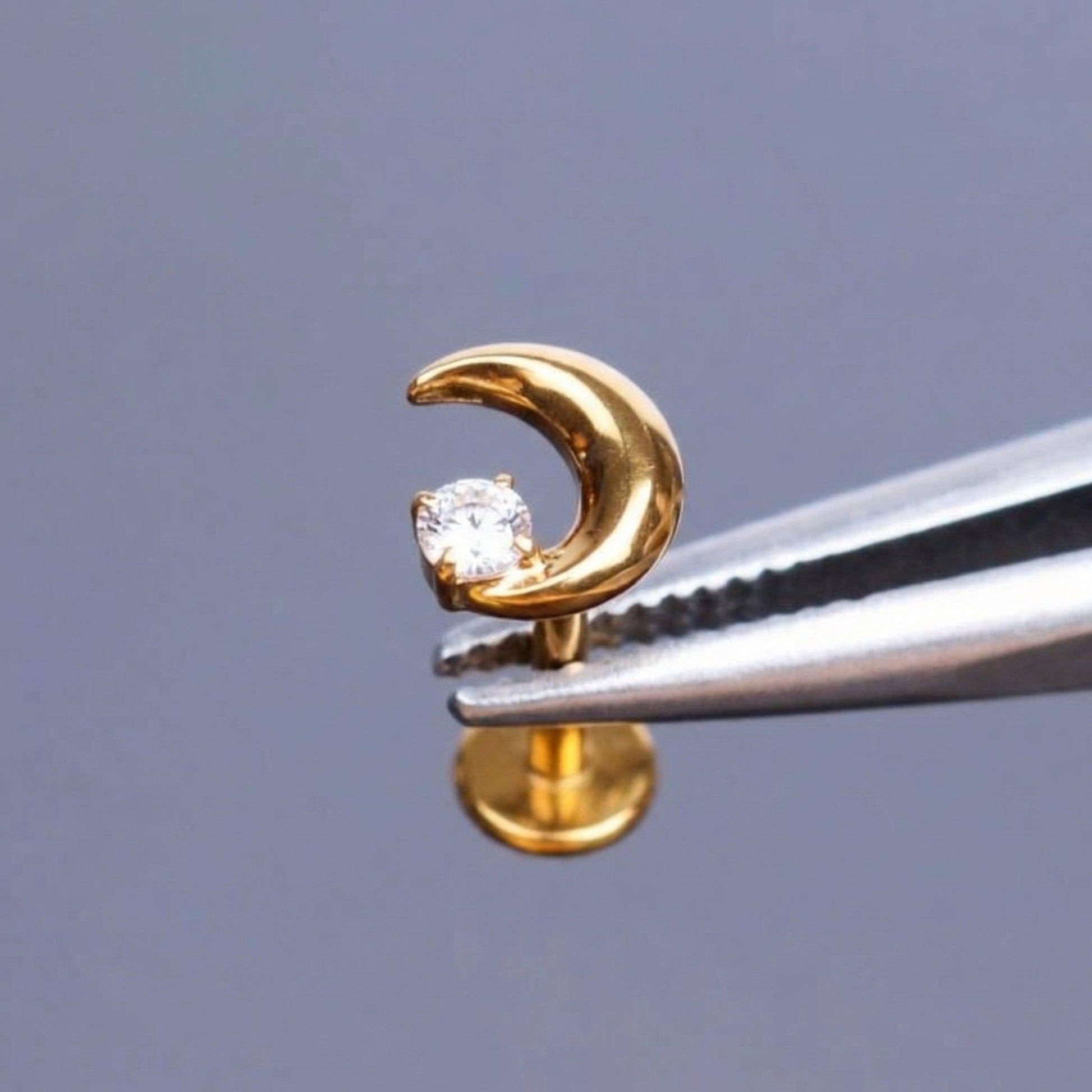 Gold crescent moon stud held securely by metal tweezers.