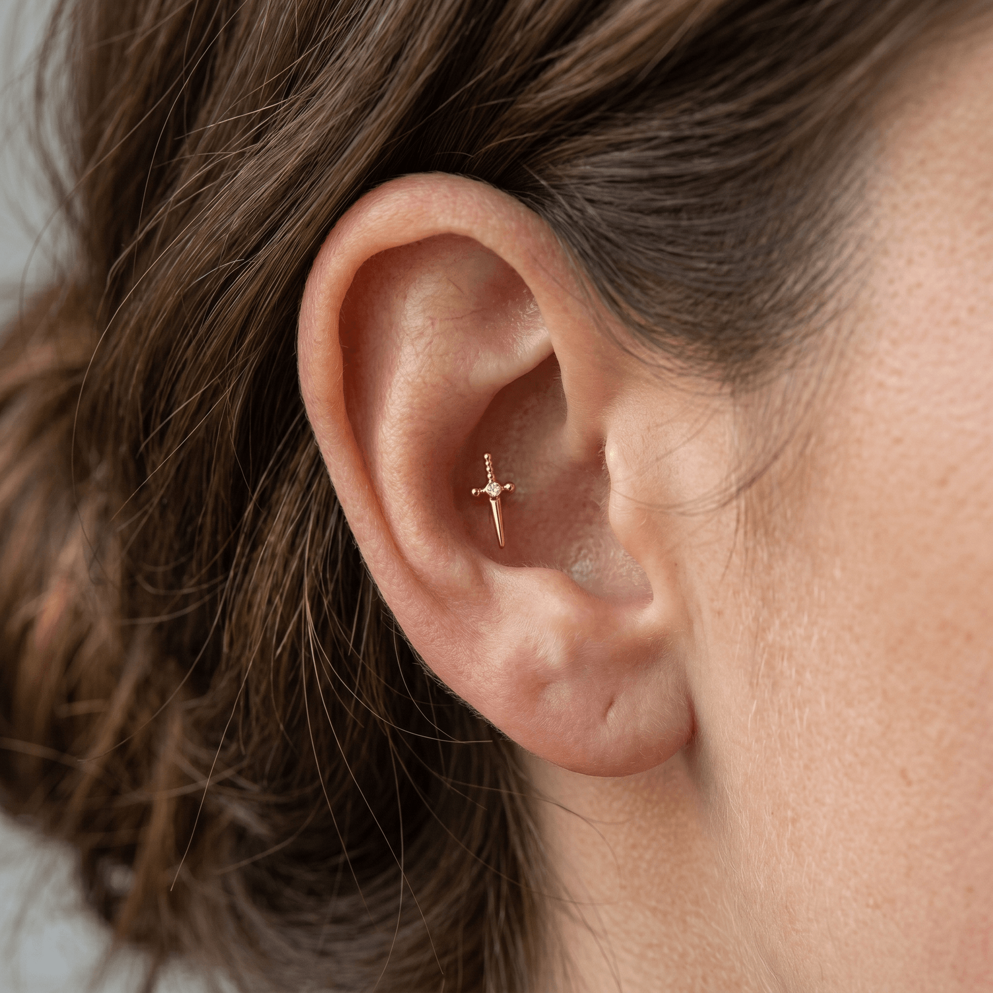 Gold dagger stud worn in a outer piercing.