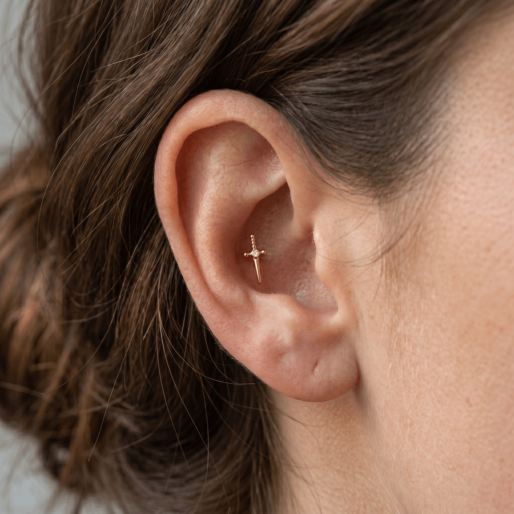 Gold dagger stud worn in a outer piercing.