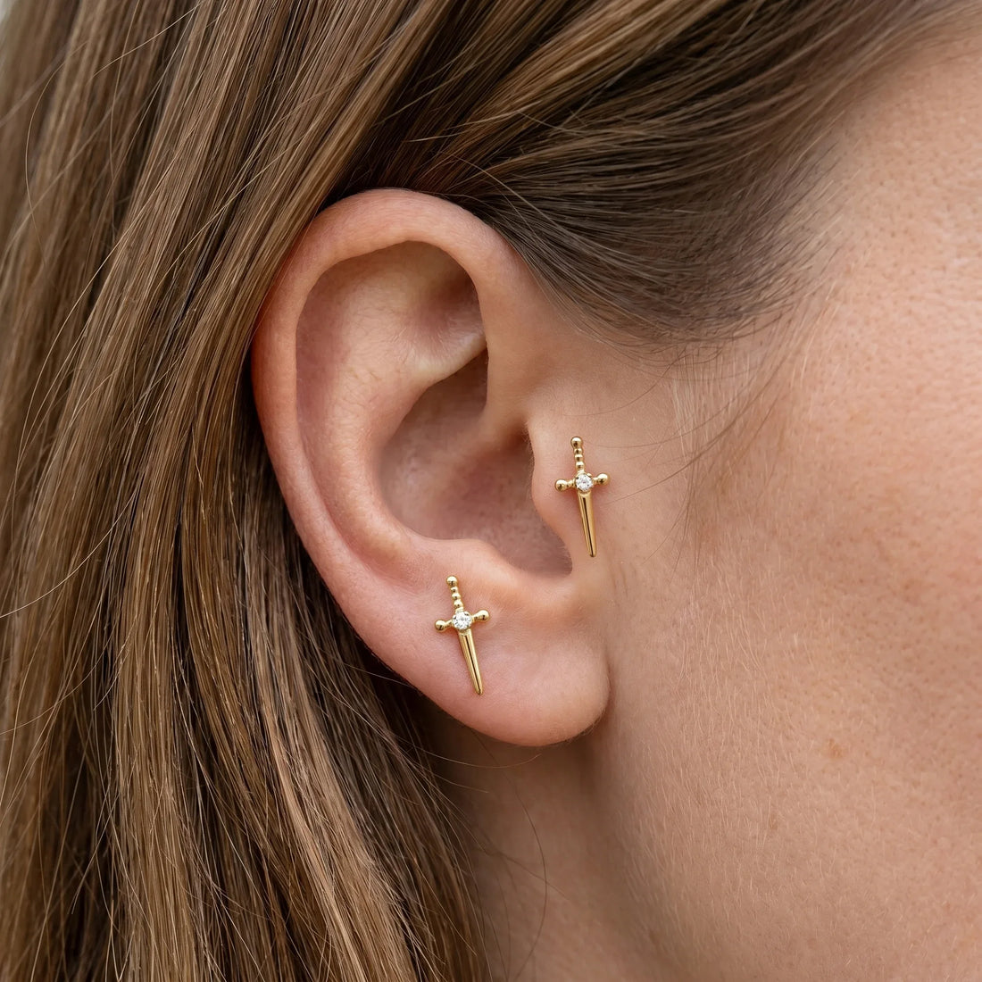 Gold dagger stud and matching stud worn beautifully in a tragus antitragus ear.
