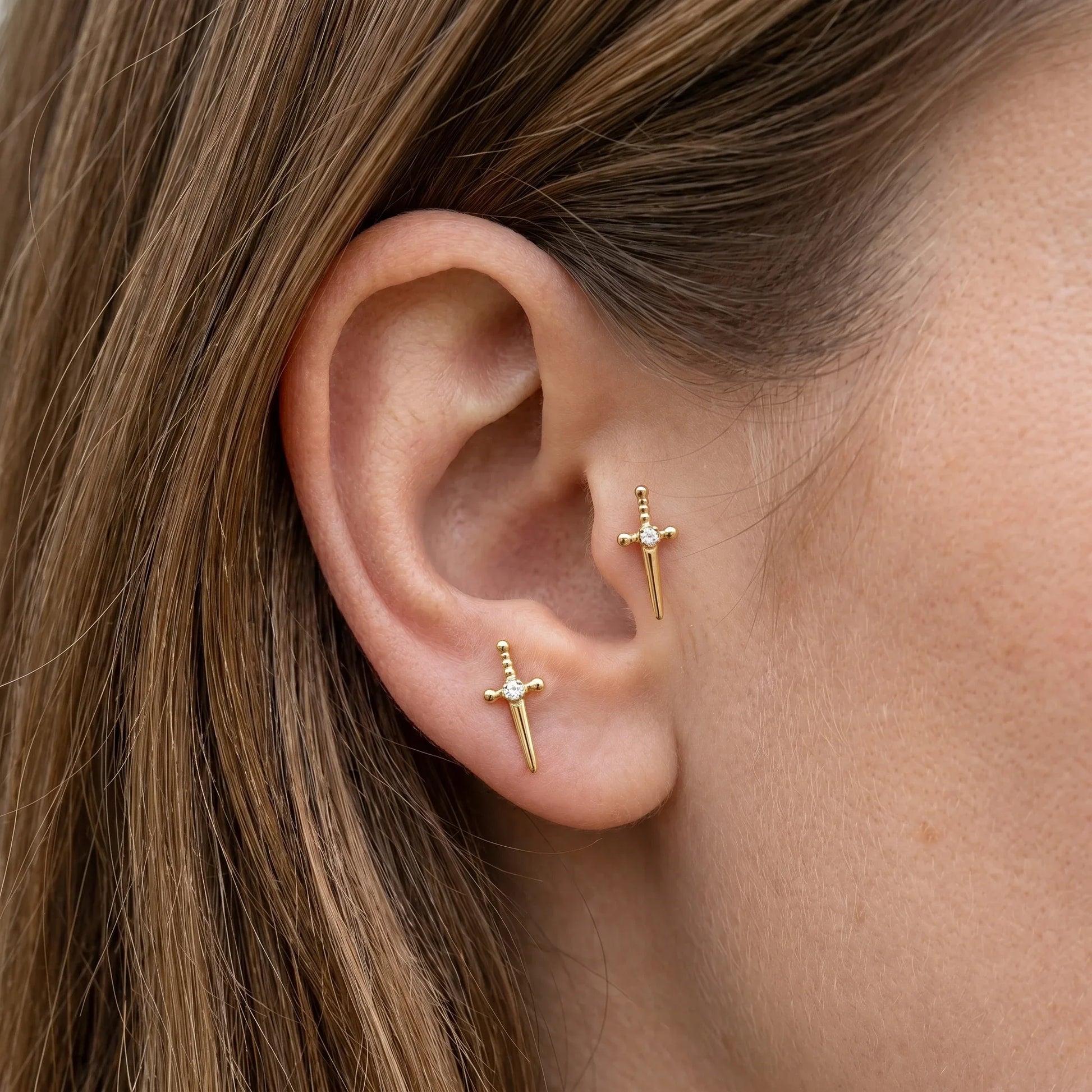 Gold dagger stud and matching stud worn beautifully in a tragus antitragus ear.