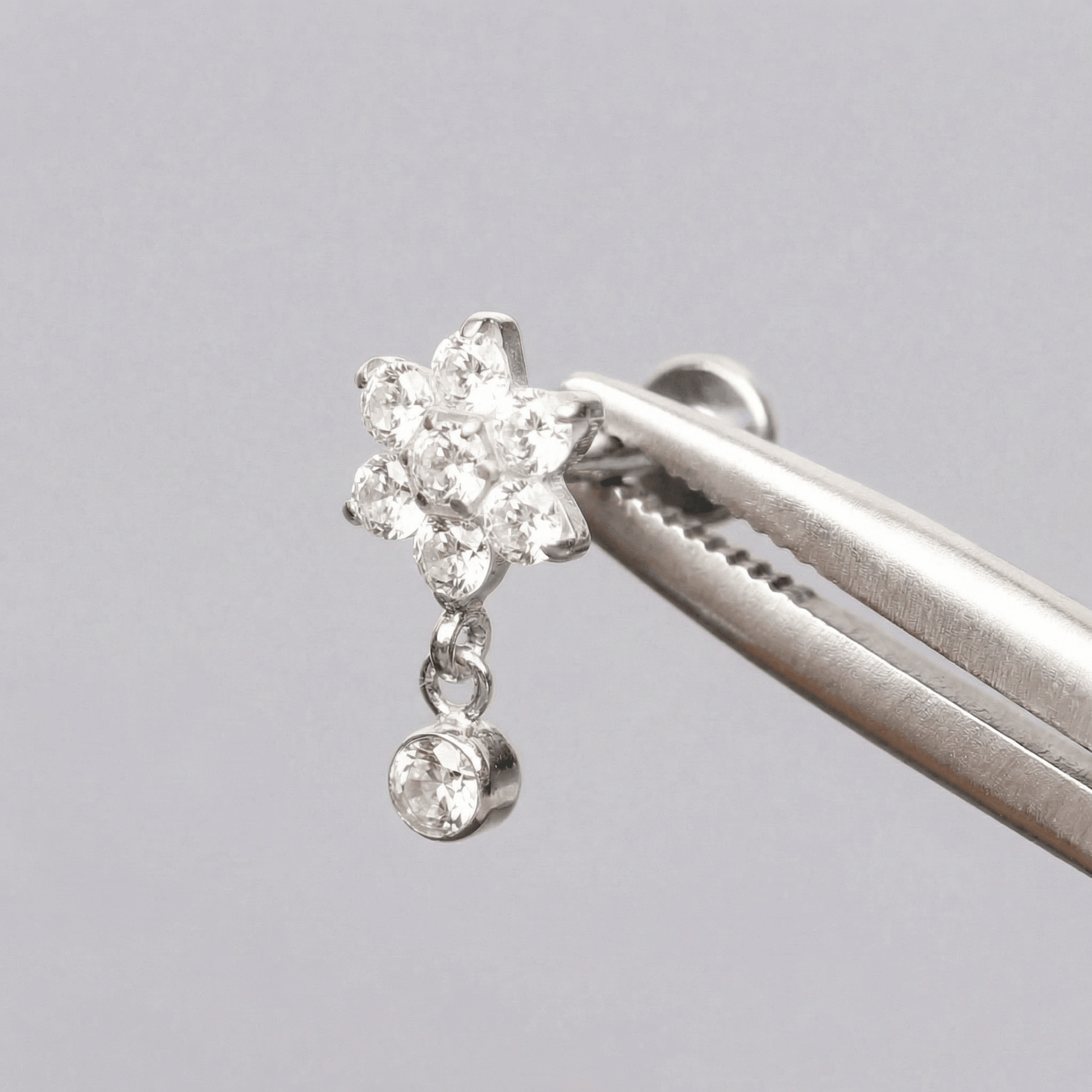 Silver daisy dangle faux stud held securely by tweezers.