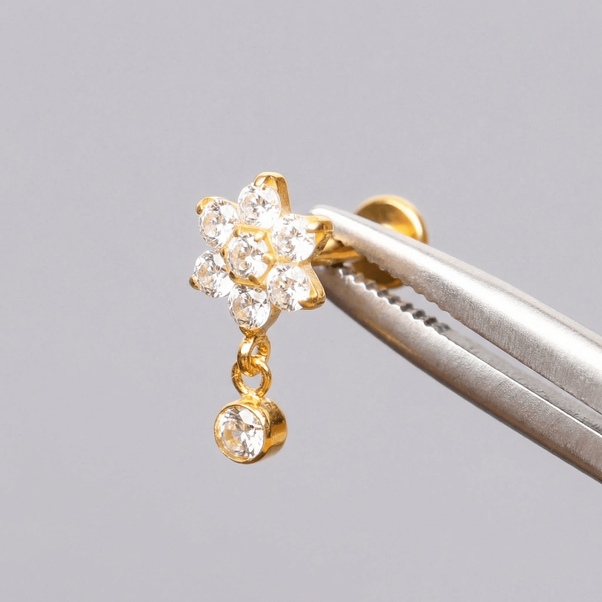 Gold titanium earring held securely by metal tweezers.