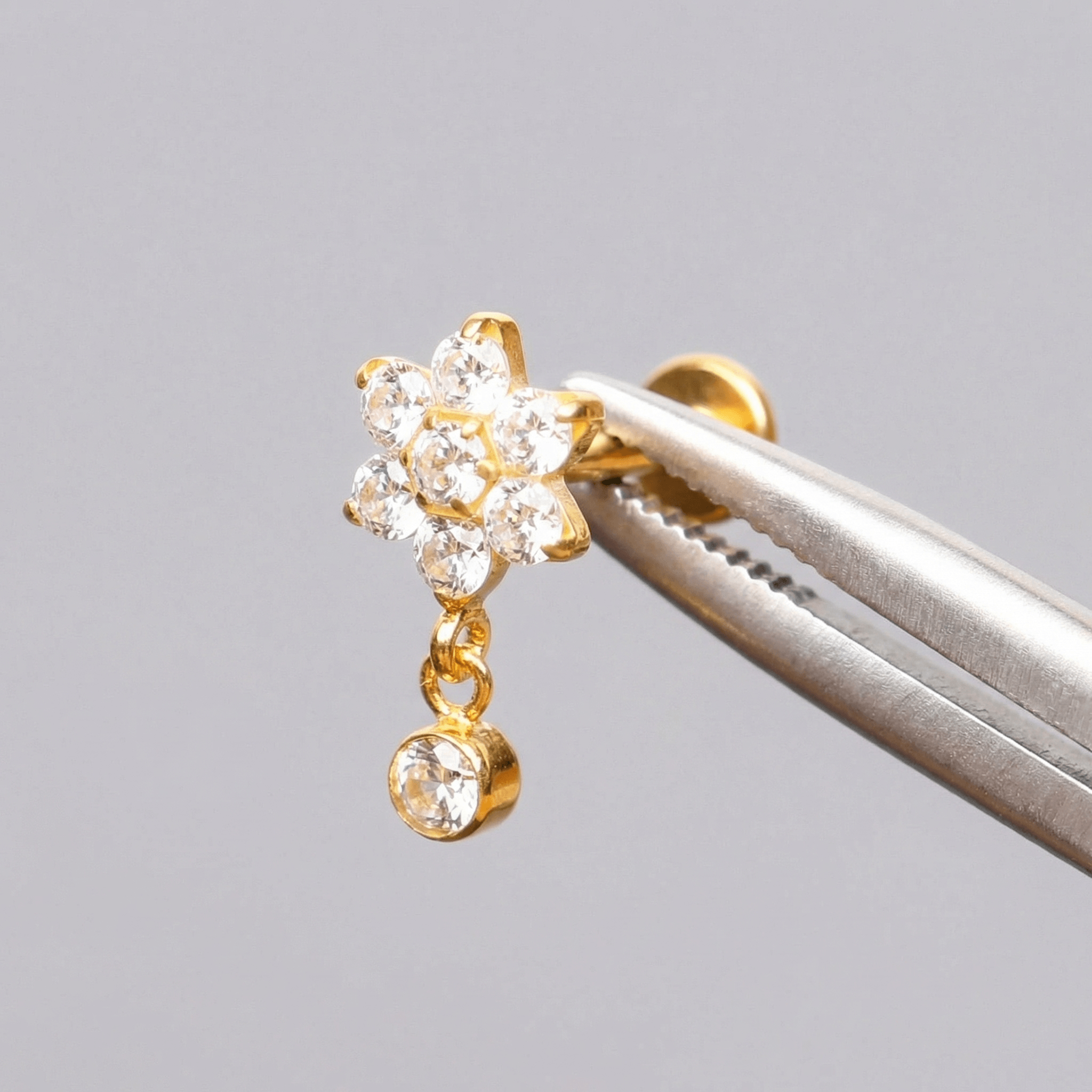 Gold titanium earring held securely by metal tweezers.