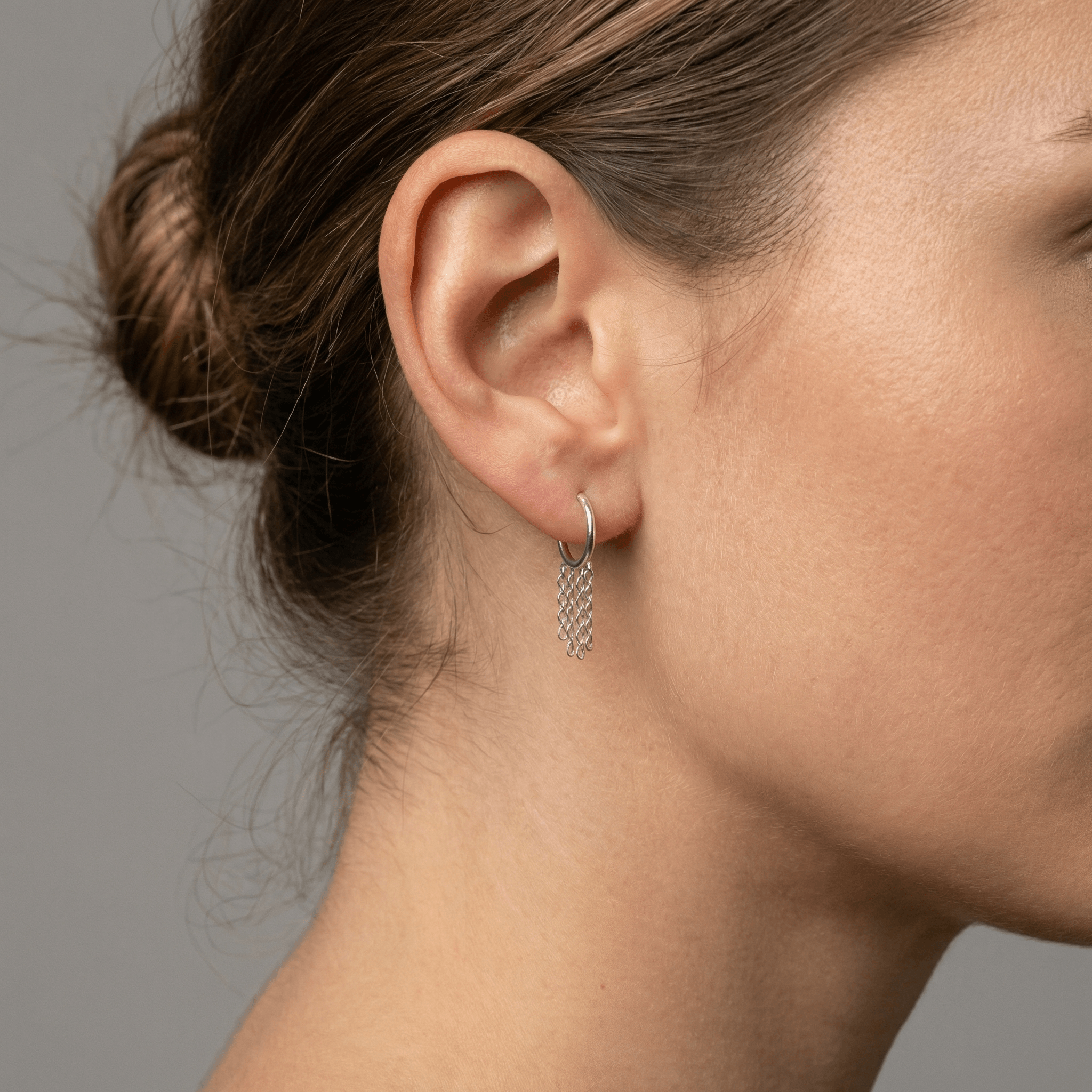 Silver dangling chain clicker hoop worn in a standard lower piercing placement