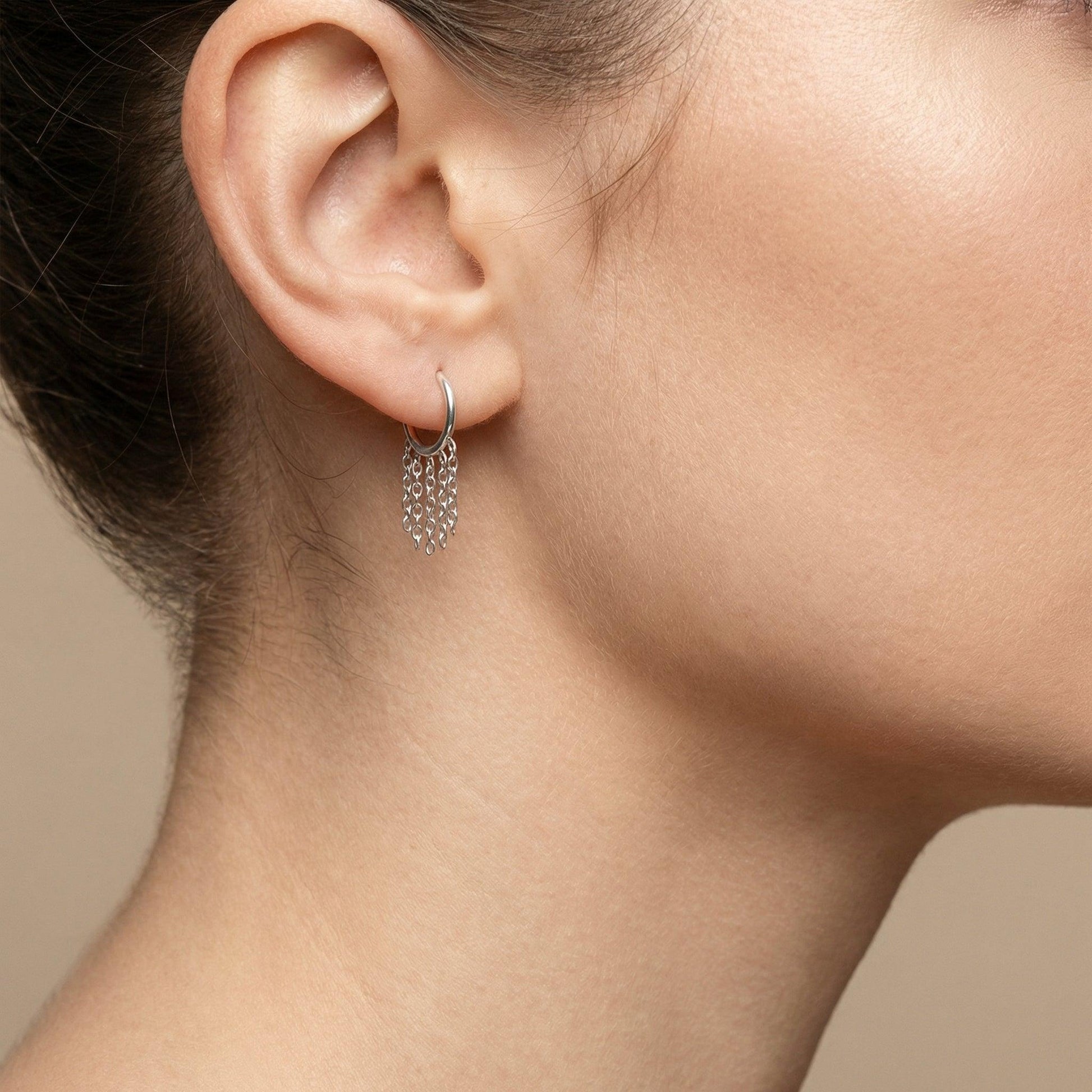 Silver dangling chain clicker hoop worn in a standard lower piercing placement