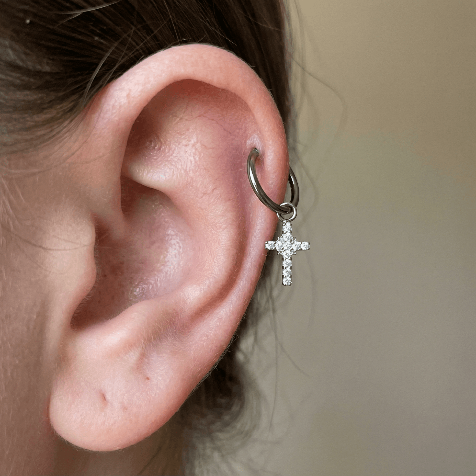 Silver cross charm titanium hoop styled in a higher ear cartilage piercing.