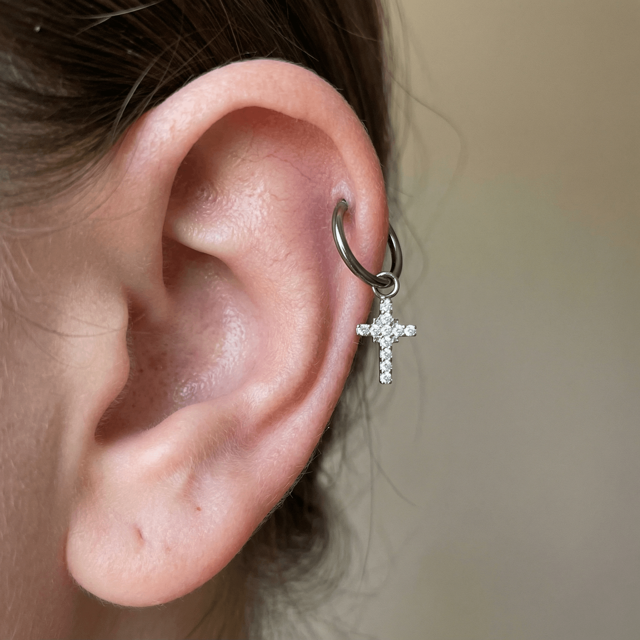 Silver cross charm titanium hoop styled in a higher ear cartilage piercing.
