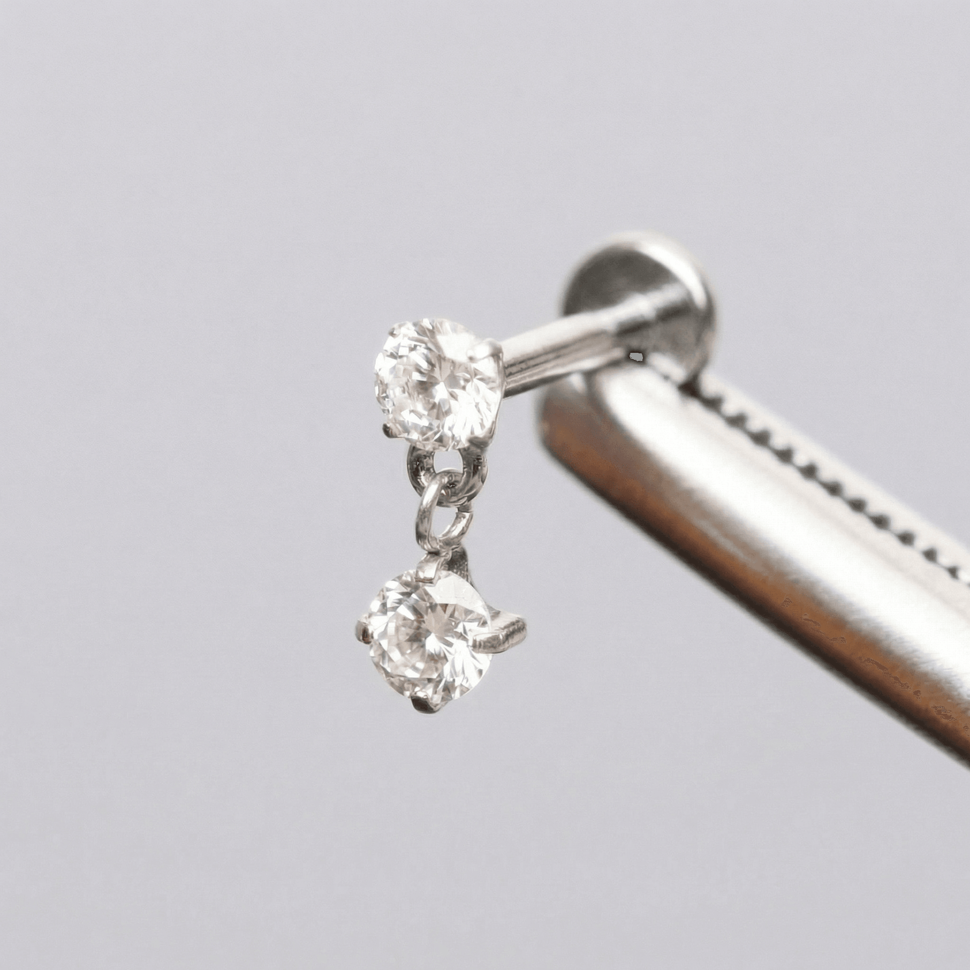 Silver double zircon stud held securely by metal tweezers.