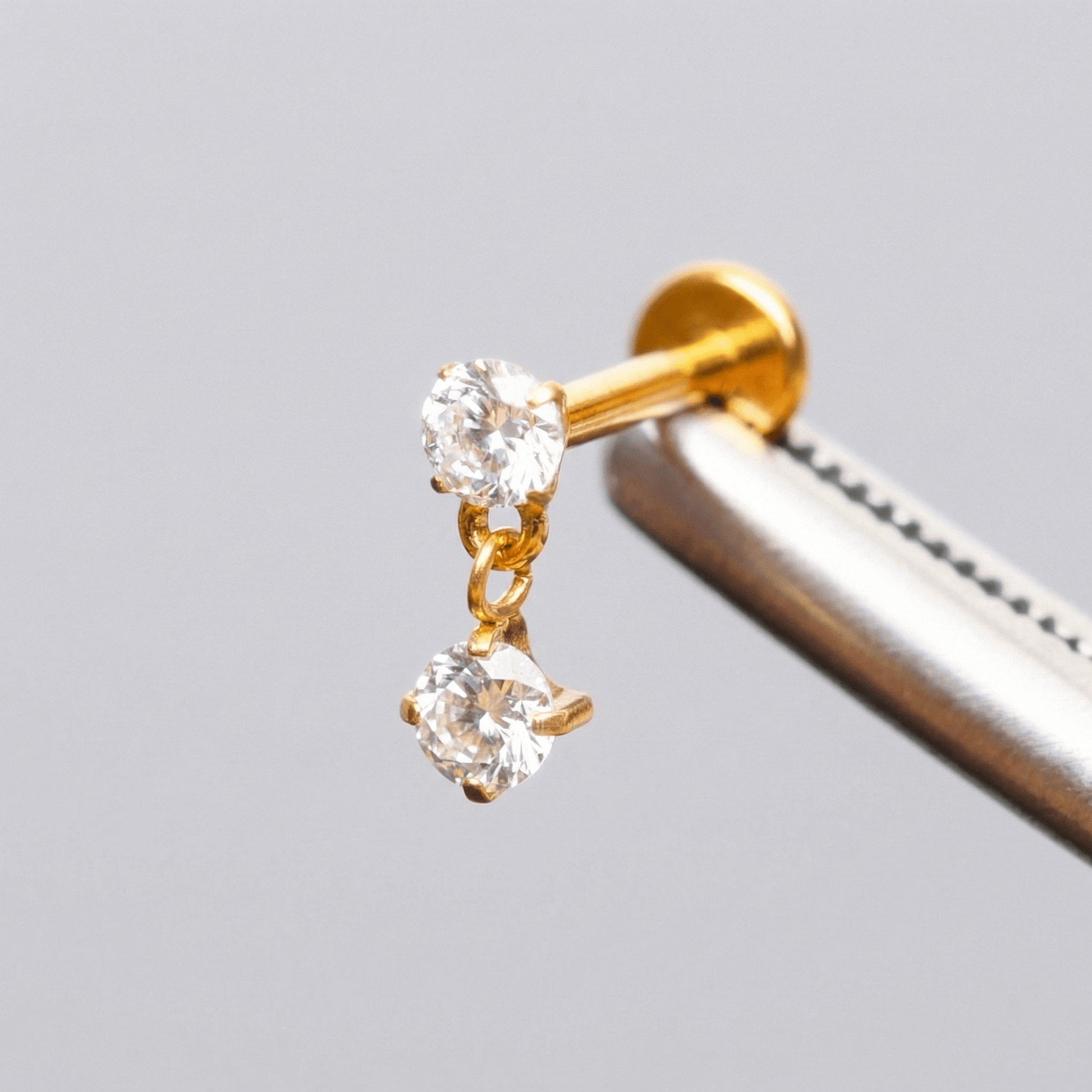 Gold double zircon stud held securely by metal tweezers.