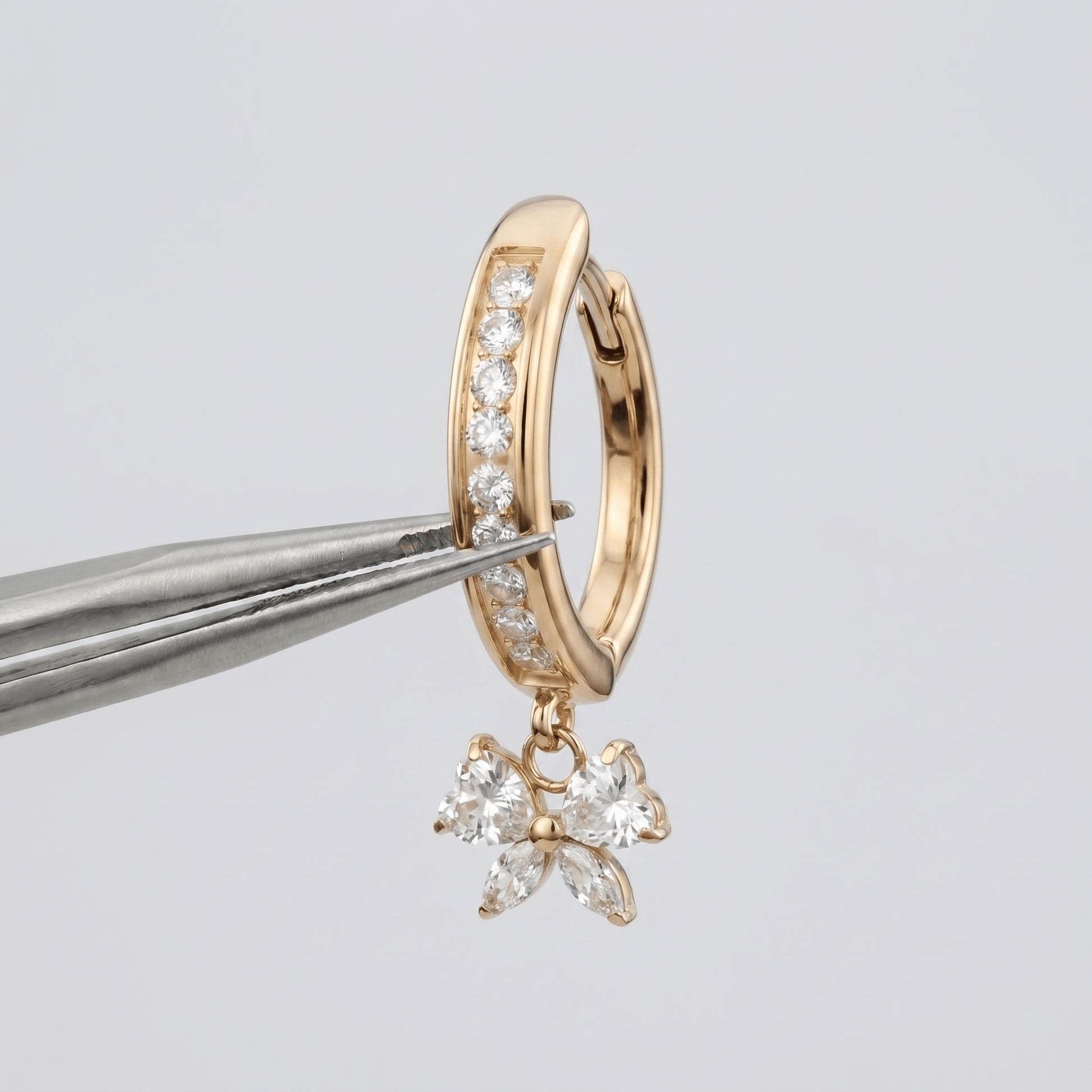 Gold dangle navel ring with cz held by tweezers.