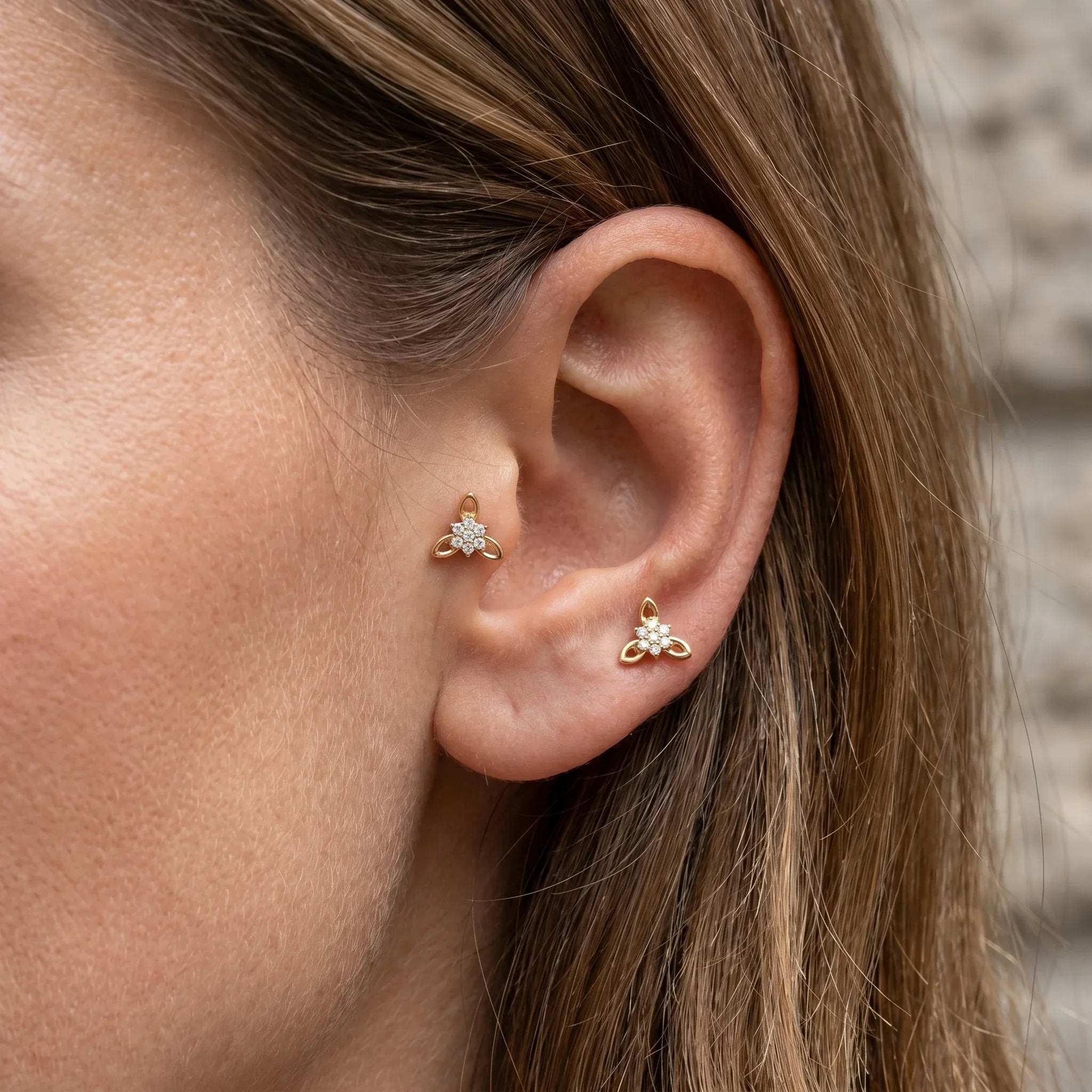 Two gold titanium CZ flower cluster piercing studs worn in a female tragus antitragus piercing.
