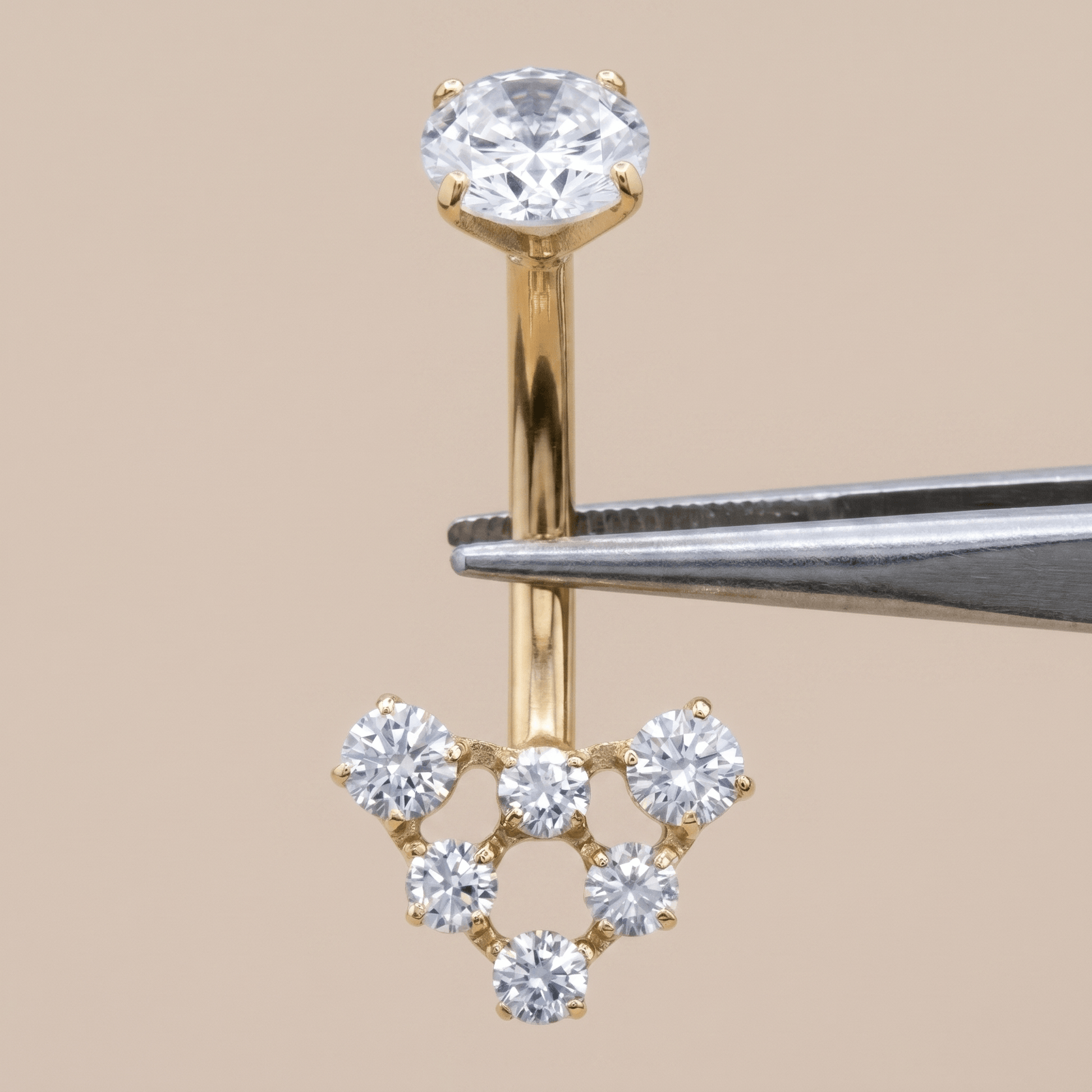 Gold 14g navel ring held securely by metal tweezers.