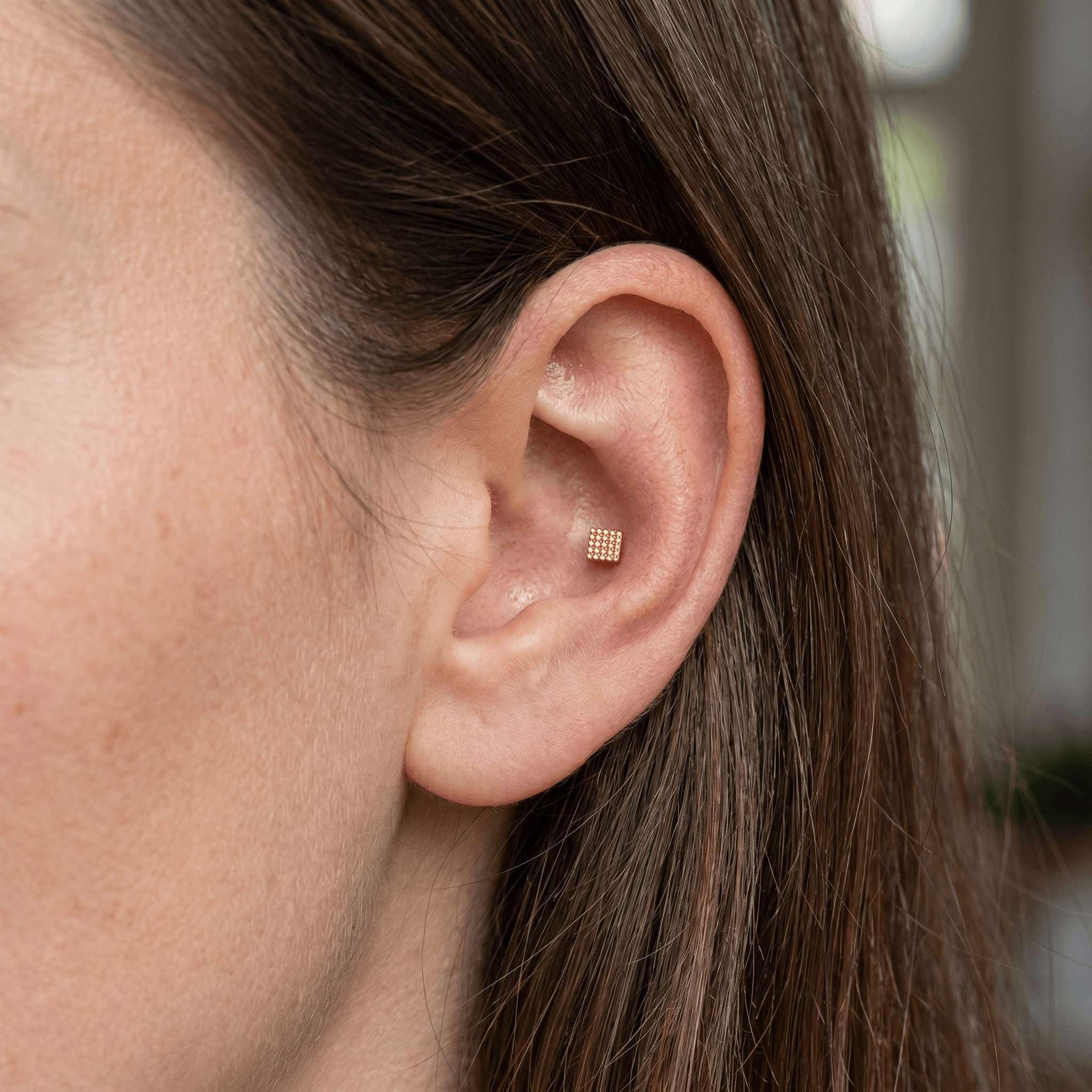 Gold geometric square titanium stud worn in a outer .