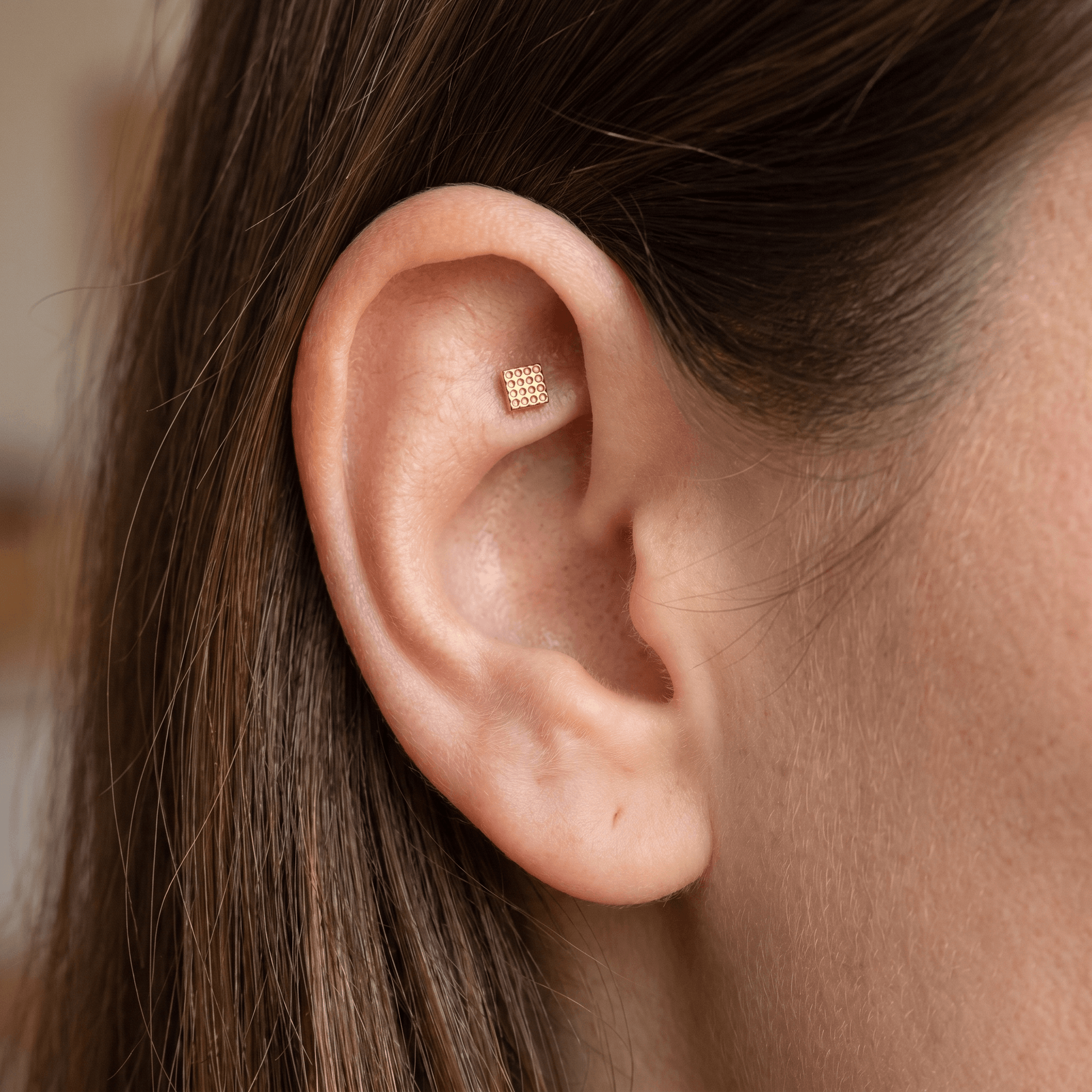 Gold geometric square faux stud worn beautifully in a female ear.